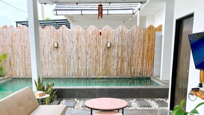 A modern outdoor seating area with a pool, a bamboo fence, and a television. - Altura Esthetic Villas (Batam)