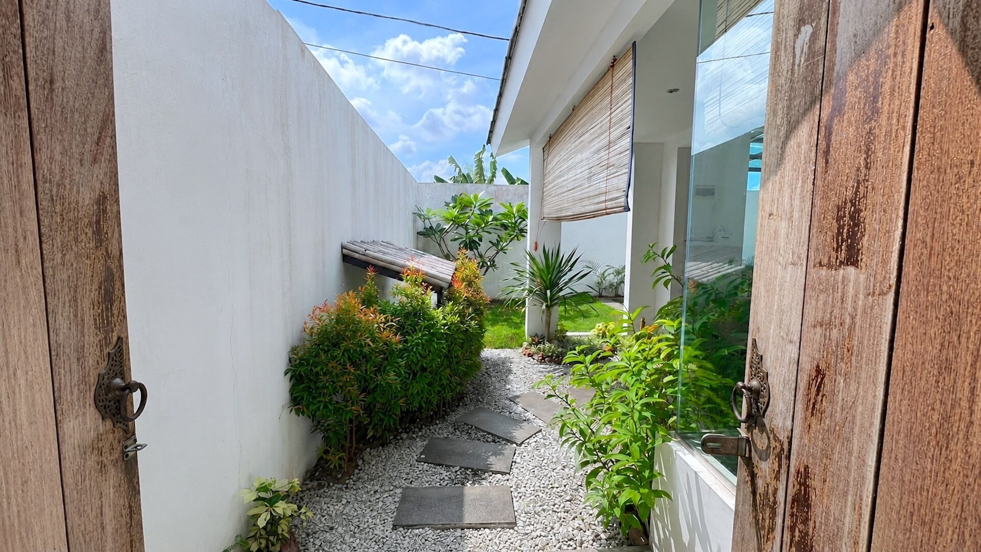 A narrow pathway leading to a modern building with a white exterior and wooden accents.