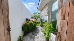 A narrow pathway leading to a modern building with a white exterior and wooden accents.