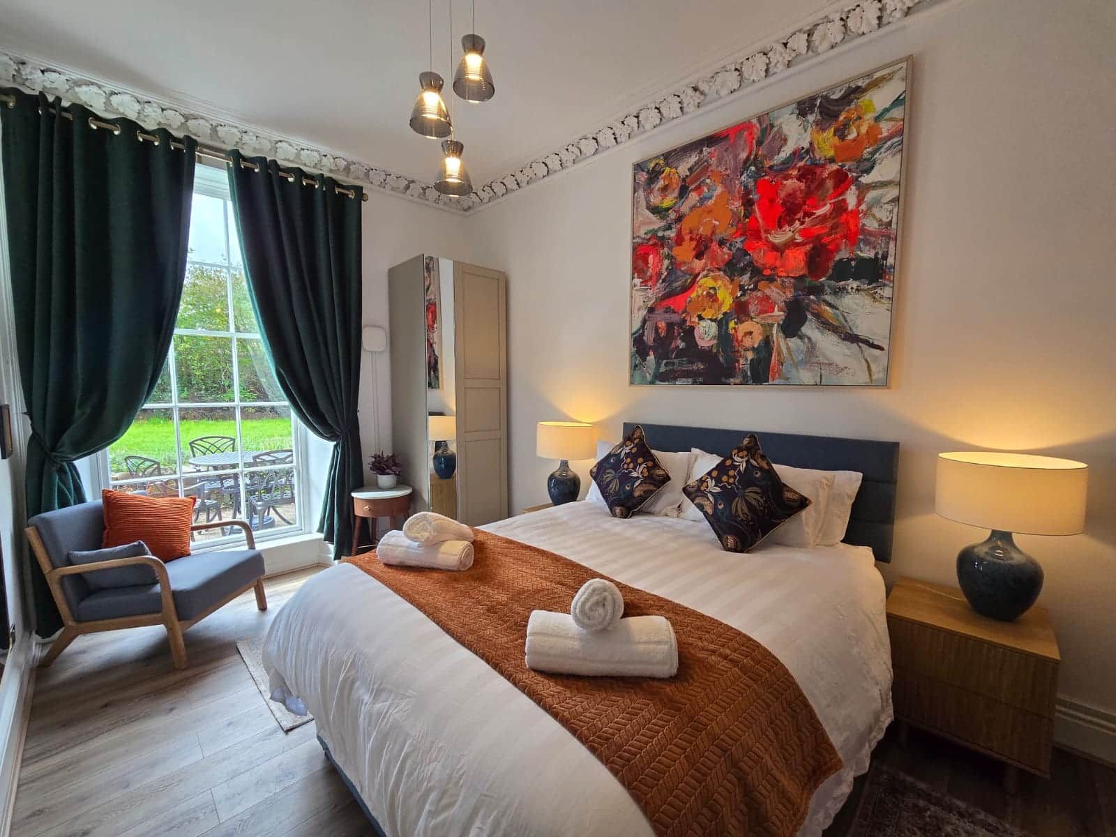 A hotel room with a large bed, two bedside lamps, a painting, and a view of the outdoors.