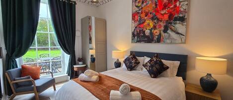 A hotel room with a large bed, two bedside lamps, a painting, and a view of the outdoors.