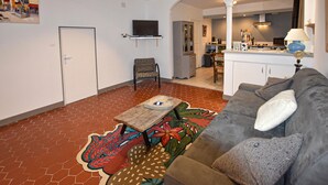 Ein Wohnzimmer mit einer Couch, einem gemusterten Teppich, einem Fernseher und einem durch einen Bogen erreichbaren Küchenbereich.