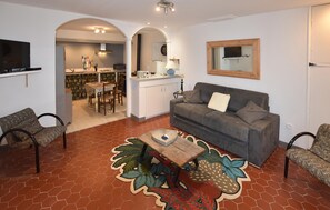 A living room with a sofa, chairs, a coffee table, and a kitchen area with a dining table. - Appart. dans maison de village (Montagnac-Montpezat)