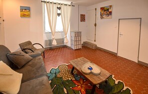Een woonkamer met een bank, een salontafel met bloemendecor, een raam met gordijnen, en kunst aan de muren.