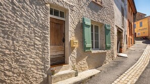 Eine enge Straße mit einem Gebäude, das eine Holztür und grüne Fensterläden sowie ein paar Stufen zum Eingang und einen gepflasterten Bürgersteig zeigt.