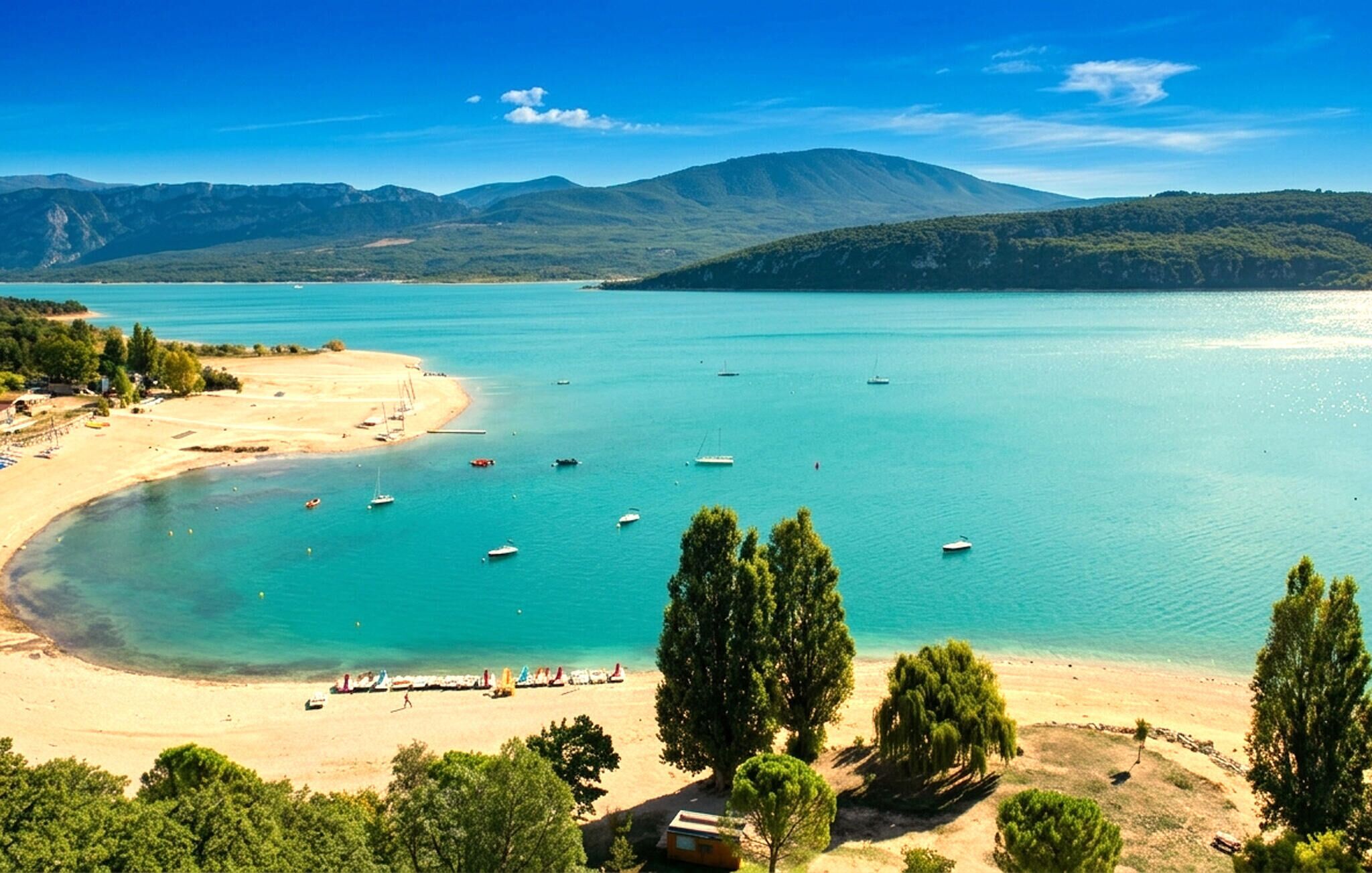 Un paysage côtier avec une plage, des bateaux et des montagnes en arrière-plan.