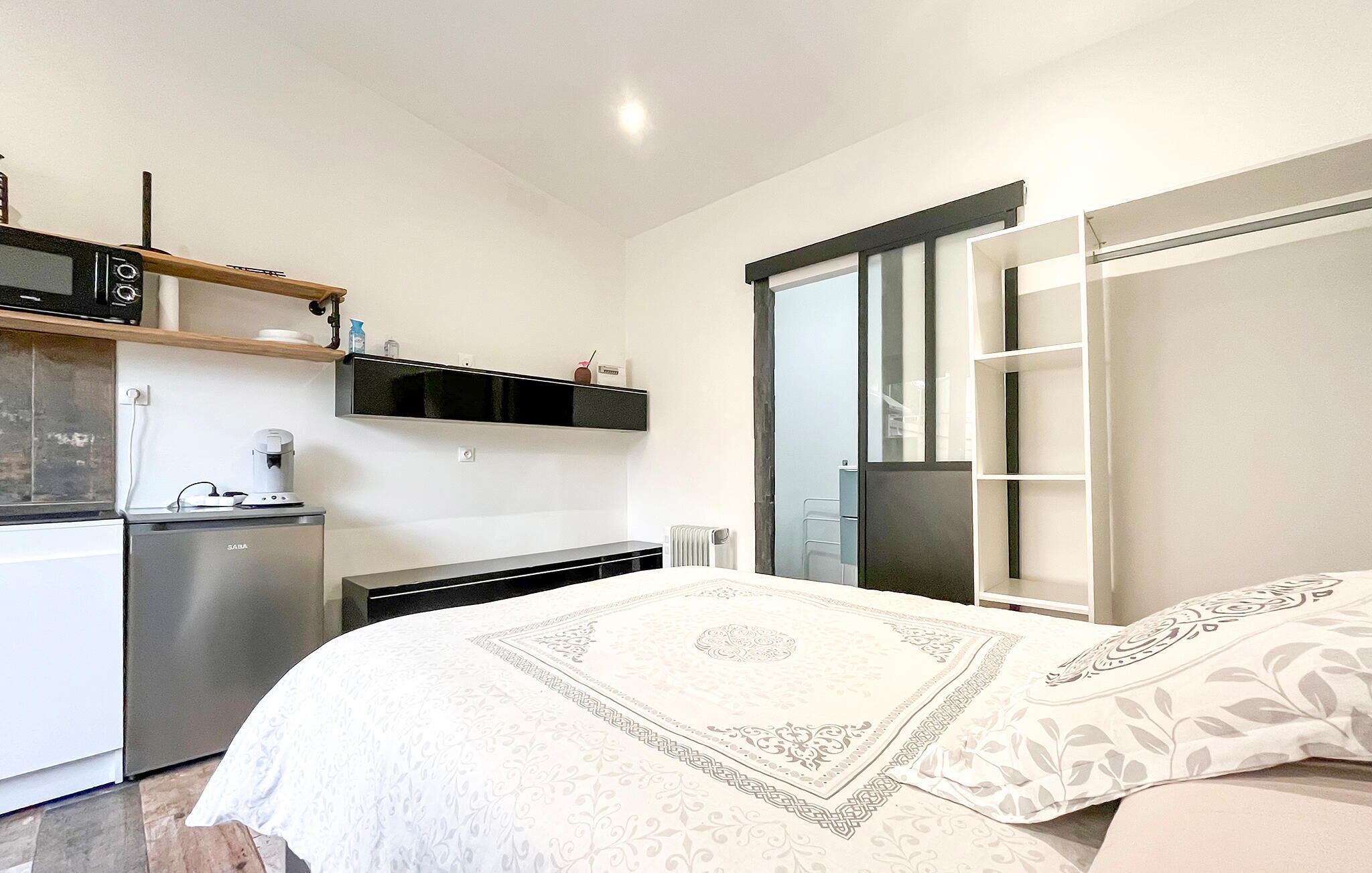 Une chambre compacte comprenant un lit, une armoire intégrée, une petite kitchenette et une grande fenêtre.