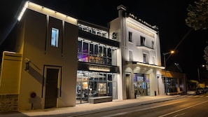 Un edifici de diverses plantes amb un cinema i un restaurant a la planta baixa, un aparcament a l'esquerra i una entrada tancada per una reixa.