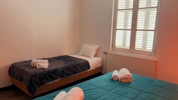 Ein Einzelbett mit dunkler Decke und Kissen, ein Fenster mit Jalousien und ein Heizkörper.