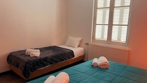 A single bed with a dark blanket and pillows, a window with blinds, and a radiator. - La Propriété de Bacchus - Écrin de Loire - Design & Confort (Saumur)
