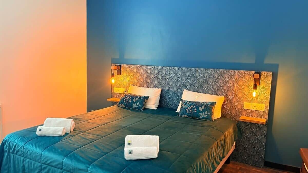 Une chambre d’hôtel avec un lit, deux tables de chevet et des lampes fixées au mur.