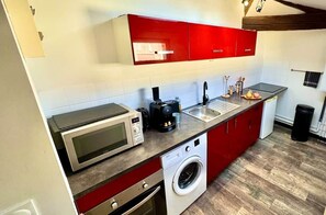 A compact kitchen with a microwave, coffee maker, sink, and a washing machine.