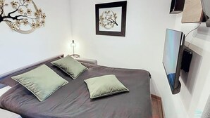 Ein Schlafzimmer mit Bett, Kissen, einem an der Wand montierten Fernseher und einem gerahmten Kunstwerk.