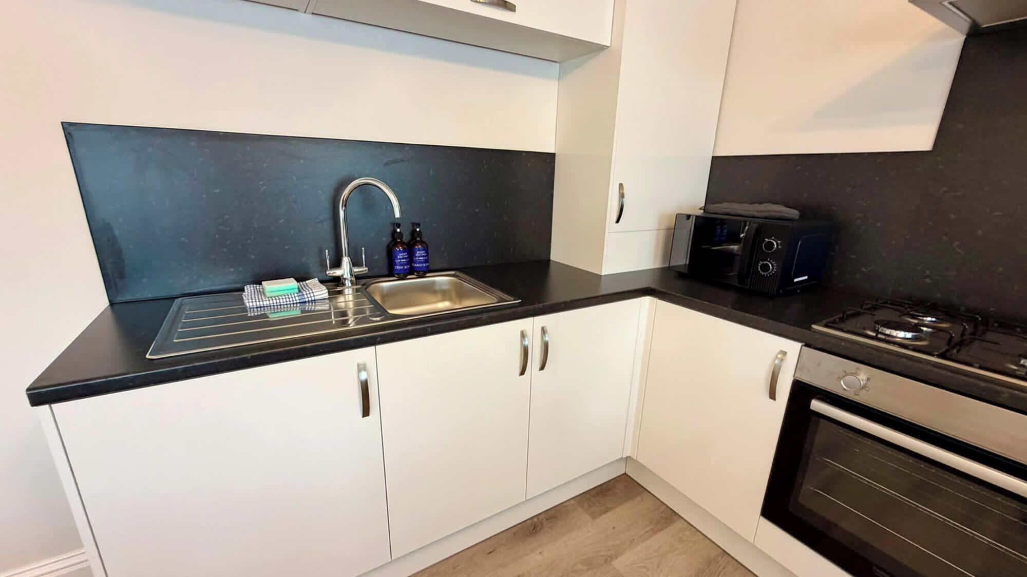 Een moderne keuken met een zwart aanrecht, een RVS-spoelbak en een ingebouwde oven.