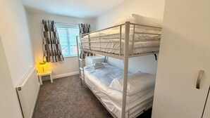 Ein Schlafraum mit Etagenbett, Fenster, Nachttisch und Heizkörper.