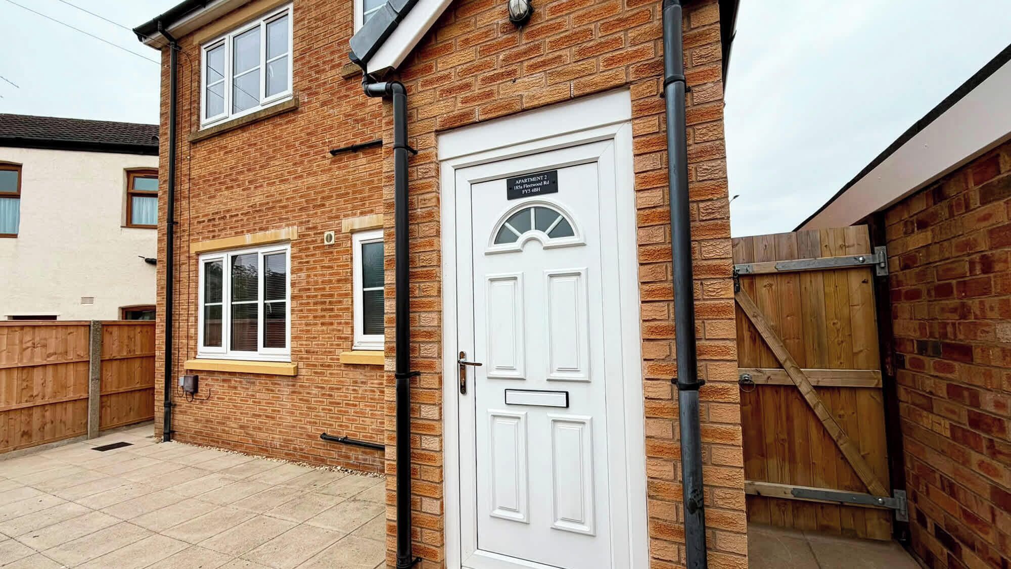 A brick house with a white door, a window, and a wooden gate.
