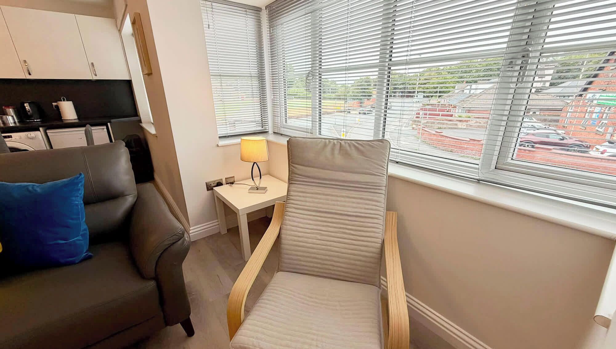 Een compacte hotelkamer met een sofa, een klein tafeltje met een lamp en een raam met zonwering.