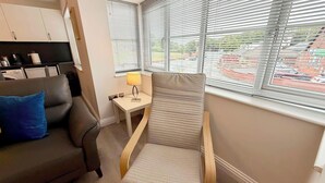 Ein gemütliches Hotelzimmer mit einer Sitzecke, einem kleinen Tisch mit Lampe und einem Fenster mit Jalousien.