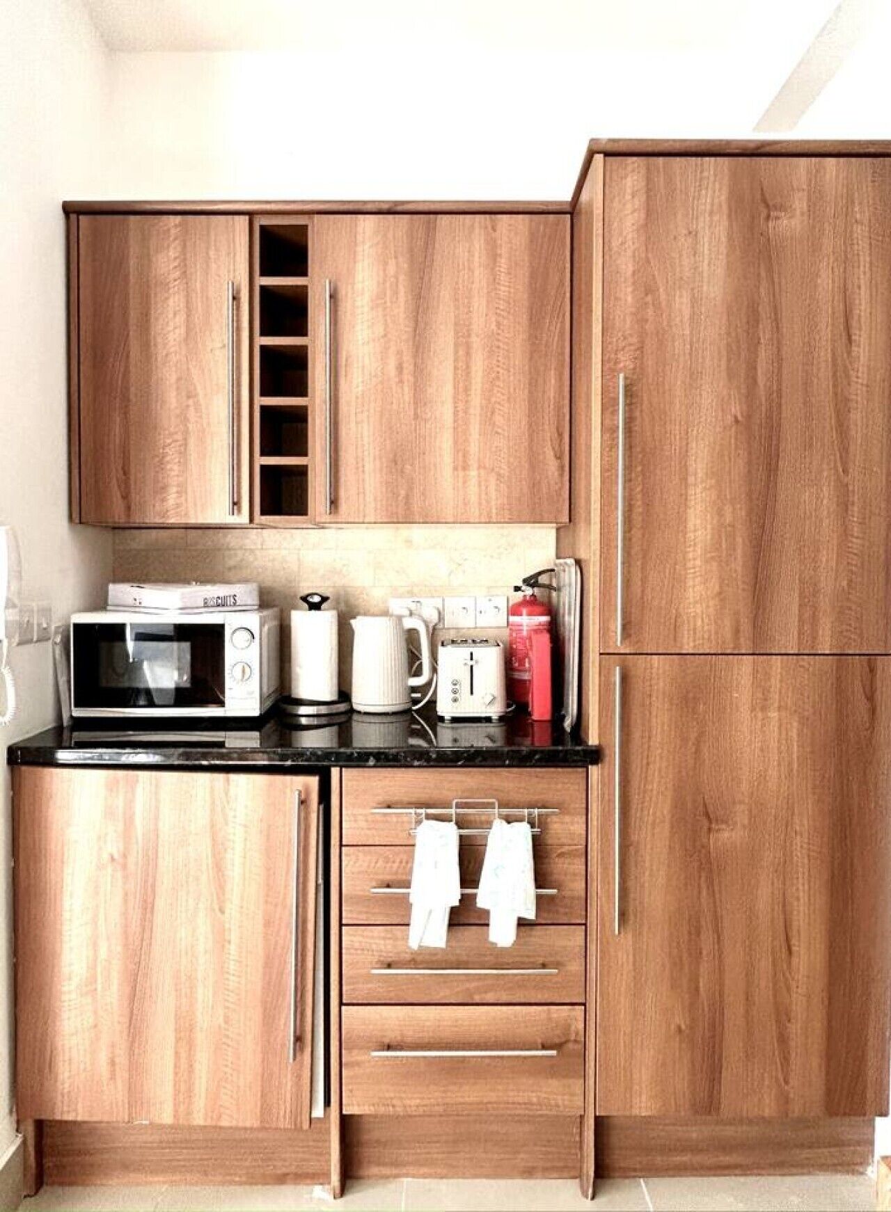 Eine kleine Küche mit Holzschränken, einer Mikrowelle, einem Wasserkocher, einem Toaster und einem roten Gerät auf der Arbeitsfläche.