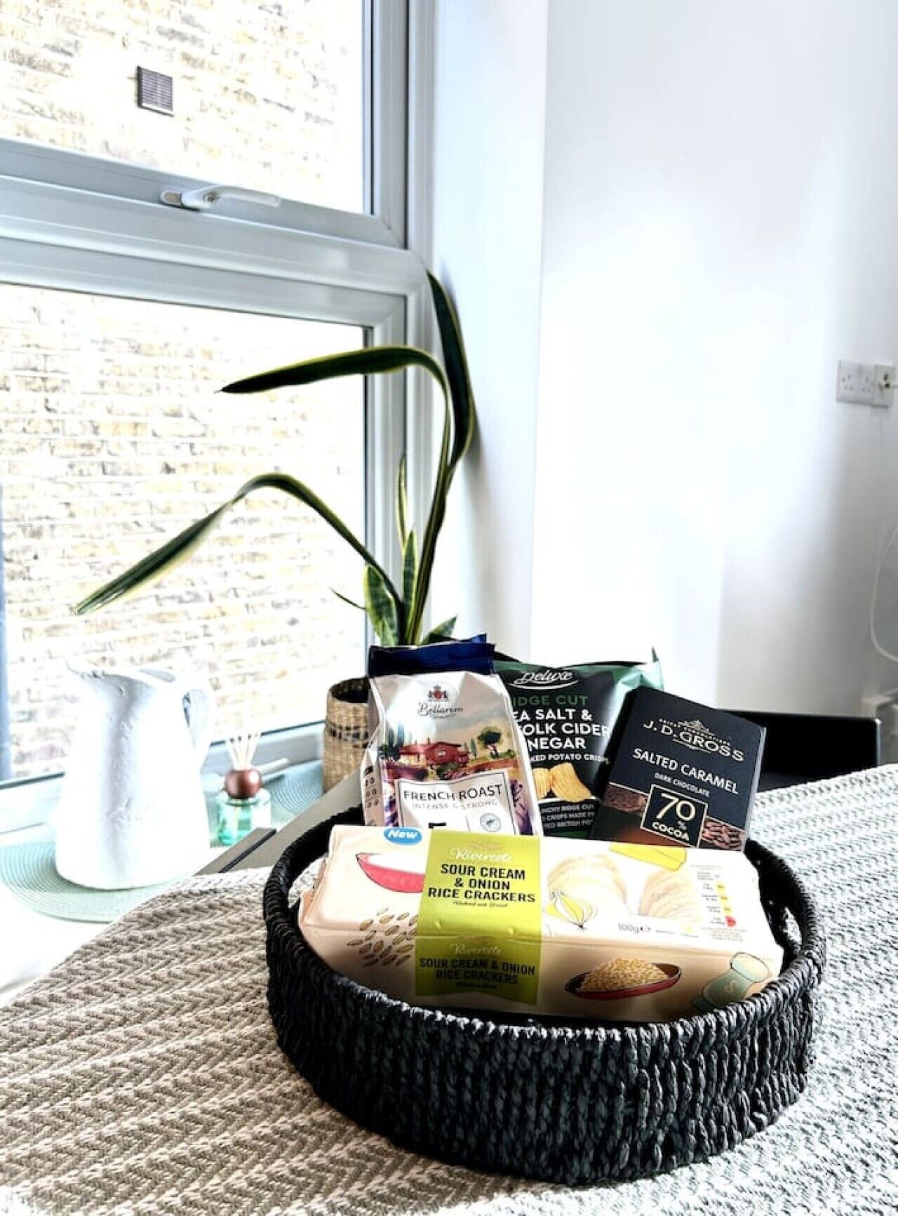 A basket containing various food items and a plant by a window.