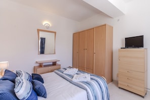 Een slaapkamer met een bed, een houten garderobe, een televisie en een spiegel.