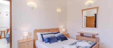 A bedroom with a bed, bedside tables, a dresser, a mirror, and wall sconces.
