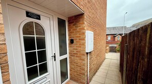 A white door with a sign above it, a brick wall, and a wooden fence. - Lower Marsh Apartment (Thornton Cleveleys)