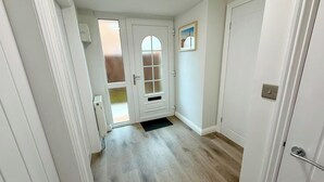 Un pasillo con una puerta que da a una habitación, un ventanal pequeño e interruptor de luz en la pared.