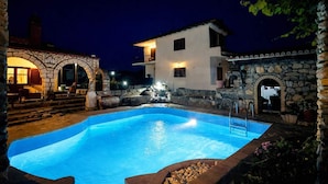 A nighttime swimming pool area with stone architecture and a fountain. - Saltos Village Apartment - Serene Poolside Escape (Nea Propontida)