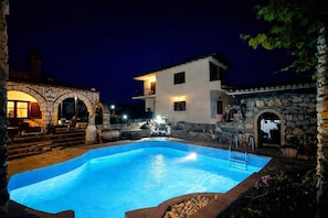 A nighttime swimming pool area with stone architecture and a fountain. - Saltos Village Apartment - Serene Poolside Escape (Nea Propontida)