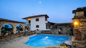 A pool area with a stone archway, a white building with a red roof, and a stone wall with a light fixture. - Saltos Village Apartment - Serene Poolside Escape (Nea Propontida)