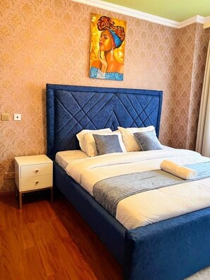 A bedroom with a bed, nightstand, and a painting on the wall. - Crestpark View Palace Apartment (Nairobi)