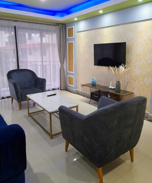 A modern living room with a flat-screen TV, a sofa, a coffee table, and a decorative vase. - Crestpark View Palace Apartment (Nairobi)