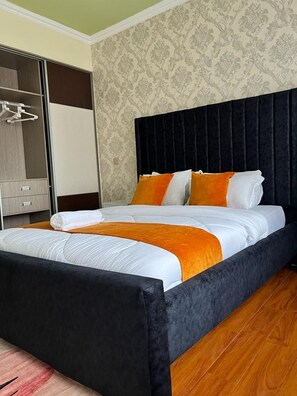 A hotel room with a large bed, a wardrobe, and a patterned wallpaper. - Crestpark View Palace Apartment (Nairobi)