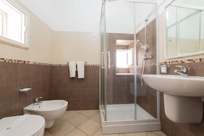 A bathroom with a shower, bidet, toilet, and sink.