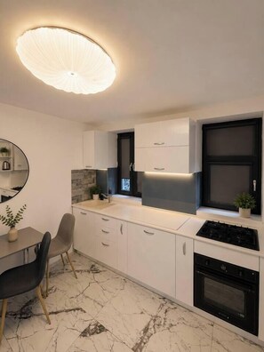 A modern kitchen with white cabinets, a black stove, and a marble floor. - Luxury Designer Studio | King Bed | Near Old Town (Bucharest)