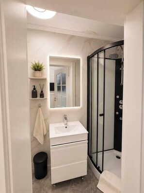 A modern bathroom with a white vanity, a glass shower enclosure, and a mirror above the sink. - Luxury Designer Studio | King Bed | Near Old Town (Bucharest)