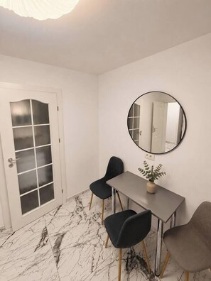 A room with a white door, a round mirror, a grey table, and two chairs. - Luxury Designer Studio | King Bed | Near Old Town (Bucharest)