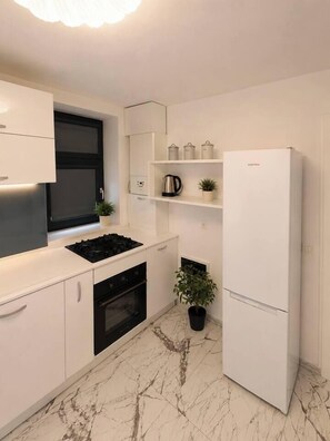 A modern kitchen with white cabinetry, a black stove, a built-in oven, a white refrigerator, and a marble floor. - Luxury Designer Studio | King Bed | Near Old Town (Bucharest)