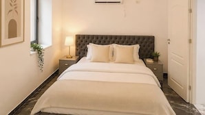 A bedroom with a tufted headboard, a bed with white bedding, a bedside table with a lamp, and a wall-mounted air conditioner. - Luxury Designer Studio | King Bed | Near Old Town (Bucharest)