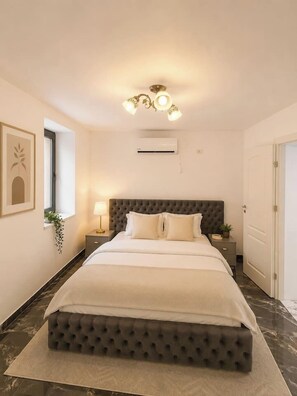 A bedroom with a tufted headboard, a bed with white bedding, a bedside table with a lamp, and a wall-mounted air conditioner. - Luxury Designer Studio | King Bed | Near Old Town (Bucharest)