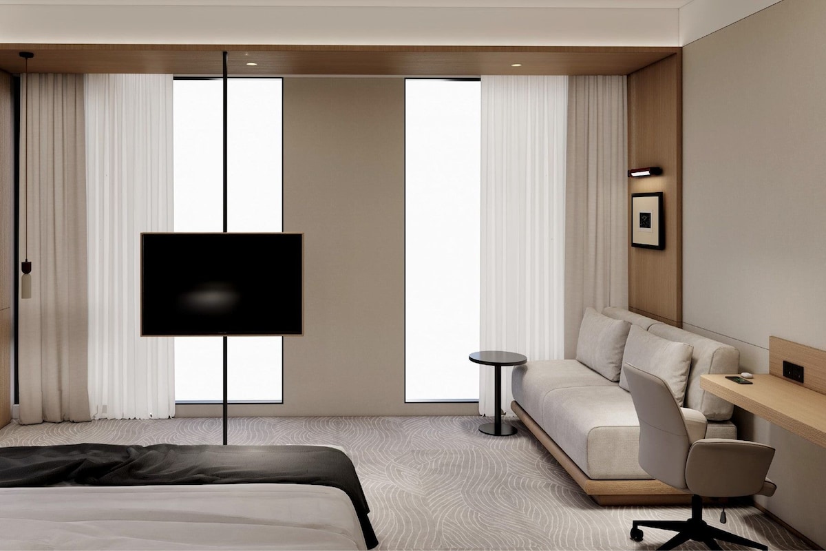 A modern hotel room with a bed, a sofa, a desk, a TV, and a small table.