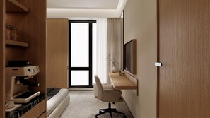 A hotel room with a kitchenette, a bed, a desk with a chair, a television, and a large window.
