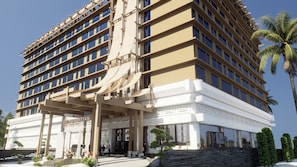 A multi-story hotel with a modern architectural design, featuring a prominent entrance with a covered walkway and a landscaped area with palm trees and shrubs.