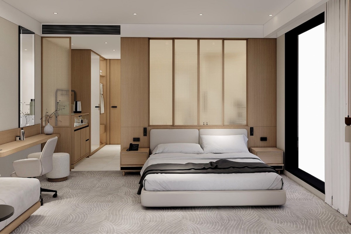 A modern hotel bedroom with a large bed, bedside tables, a desk, and a mirror.