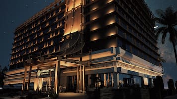 Un hotel de varios pisos con una entrada imponente, un letrero visible del Manhattan Grand Hotel y una palmera en primer plano.