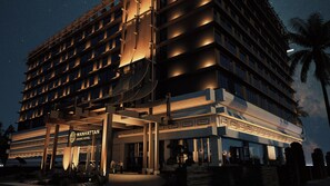 A multi-story hotel with a grand entrance, a visible sign for the Manhattan Grand Hotel, and a palm tree in the foreground.