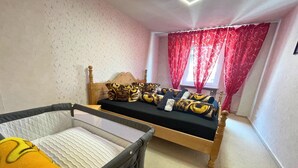 Un dormitorio con cama, ventana con cortinas rojas y cuna con cobija amarilla.