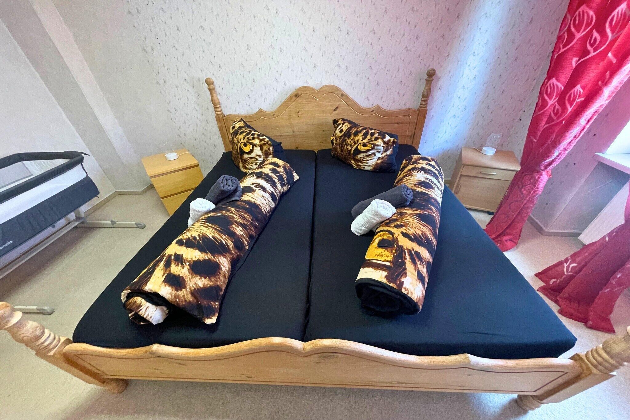 Ein Bett mit Holzrahmen, zwei Decken mit Tigerprint und ein Kopfkissen mit Tiger-Motiv.