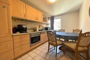 A kitchen with wooden cabinets, a coffee maker, a microwave, and a dining table with chairs. - Spacious apartment with balcony (Boppard)